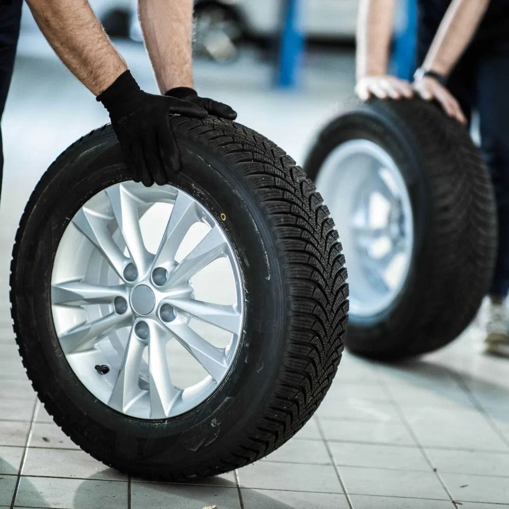 Dos personas en un garaje sosteniendo neumáticos de automóvil con llantas plateadas.