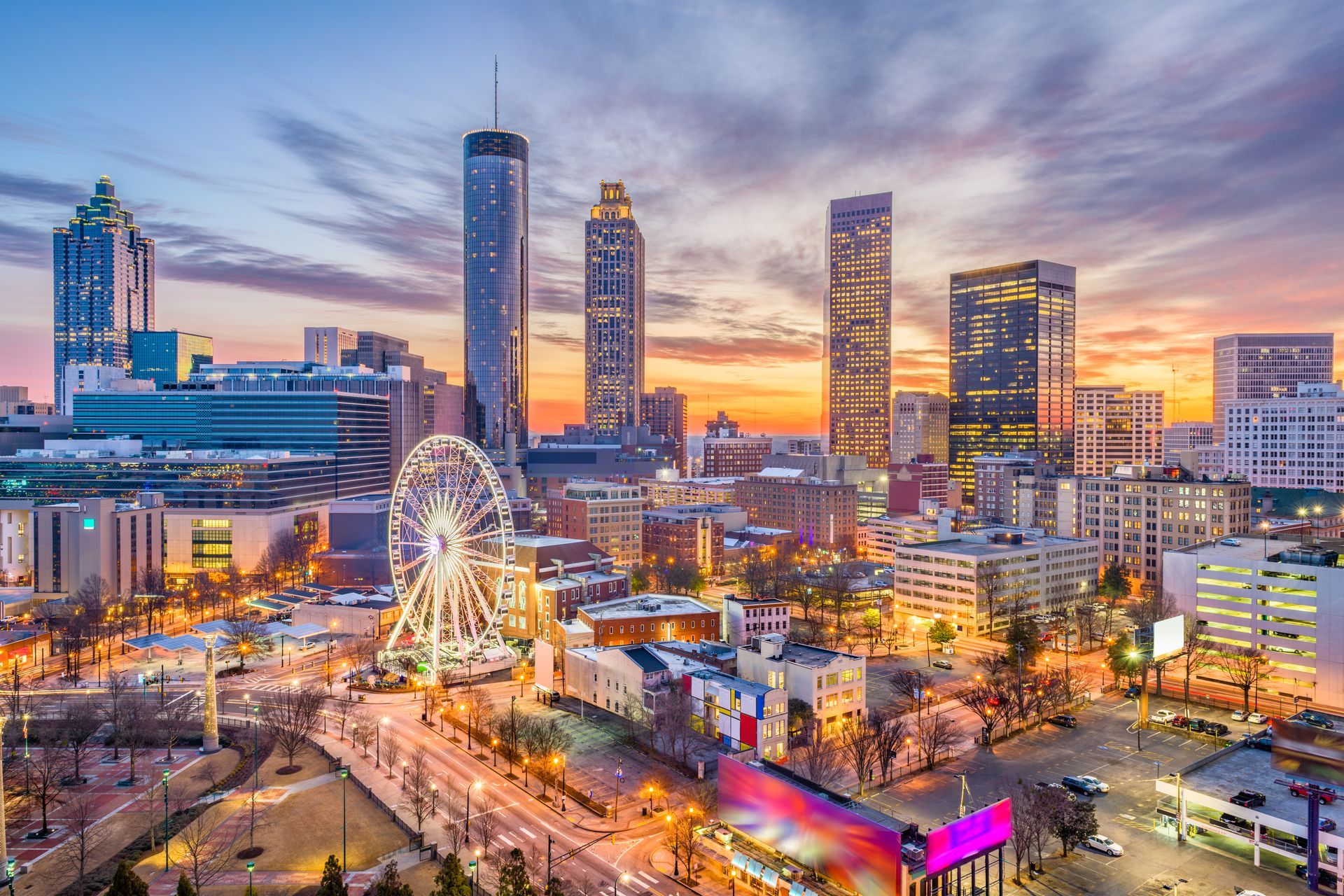 An aerial view of a city at night with a ferris wheel in the foreground.