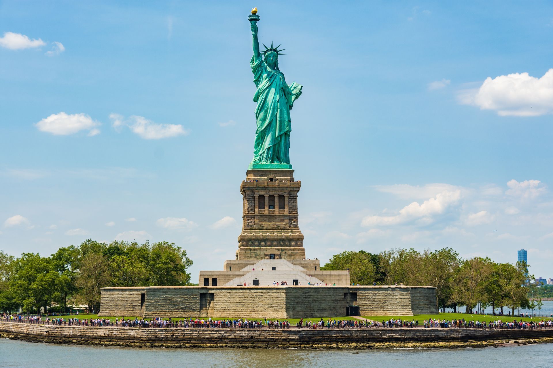 The statue of liberty is sitting on top of a small island in the middle of a body of water.