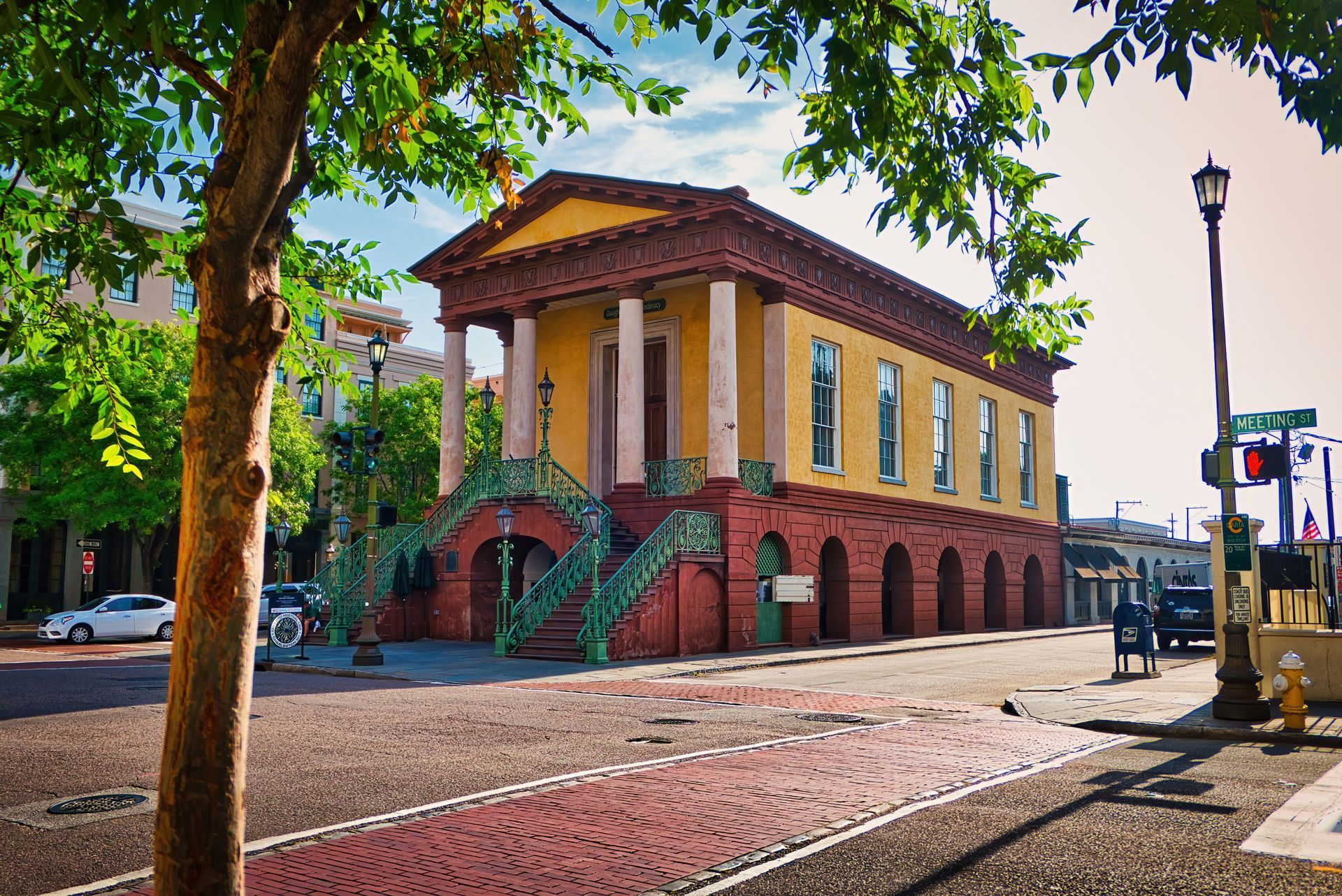 A large yellow building with columns is sitting on the corner of a brick street.