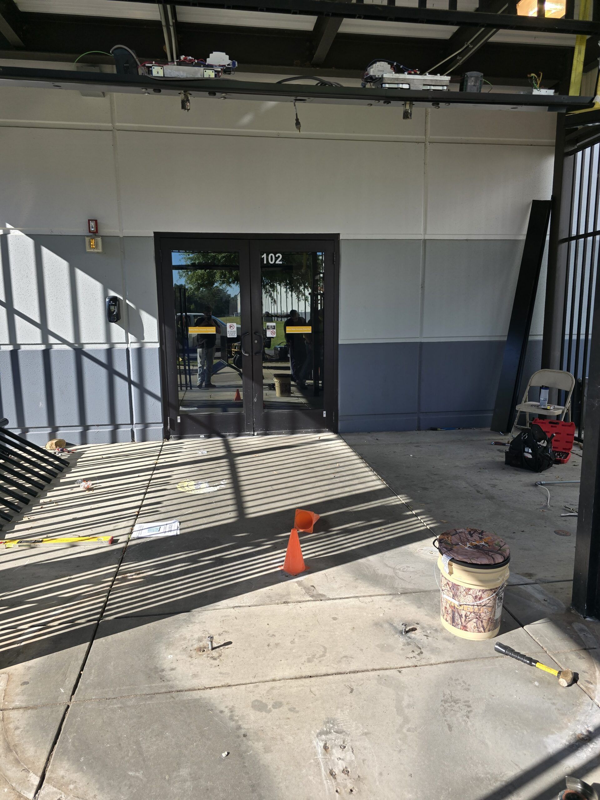 Exterior of building with double doors, ramp, and construction materials. Gray walls with blue accent.