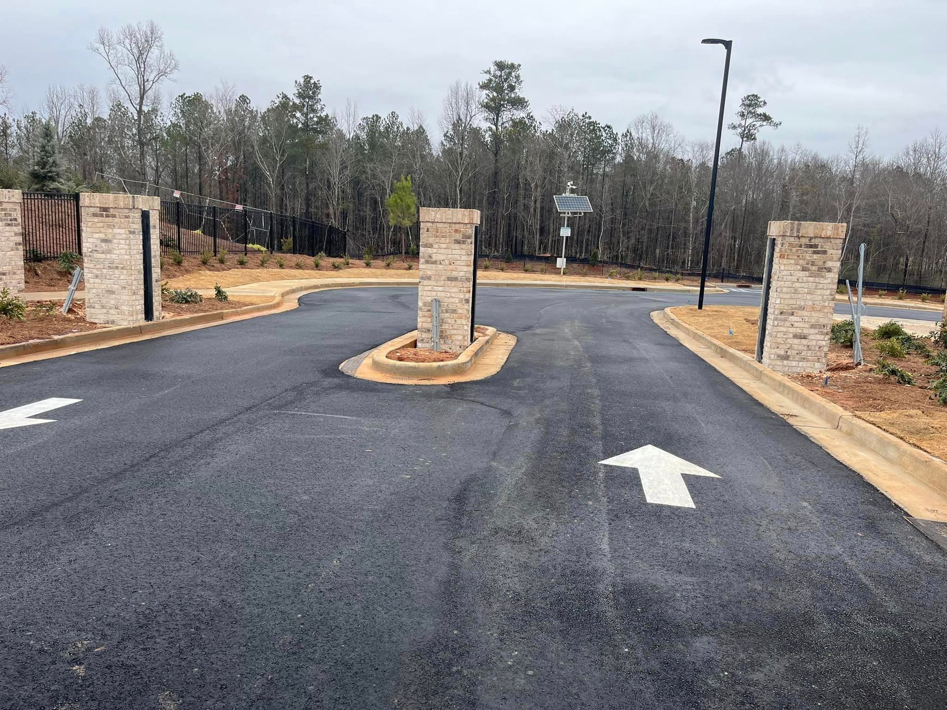 Asphalt road with white arrows, brick pillars, and wooded background.