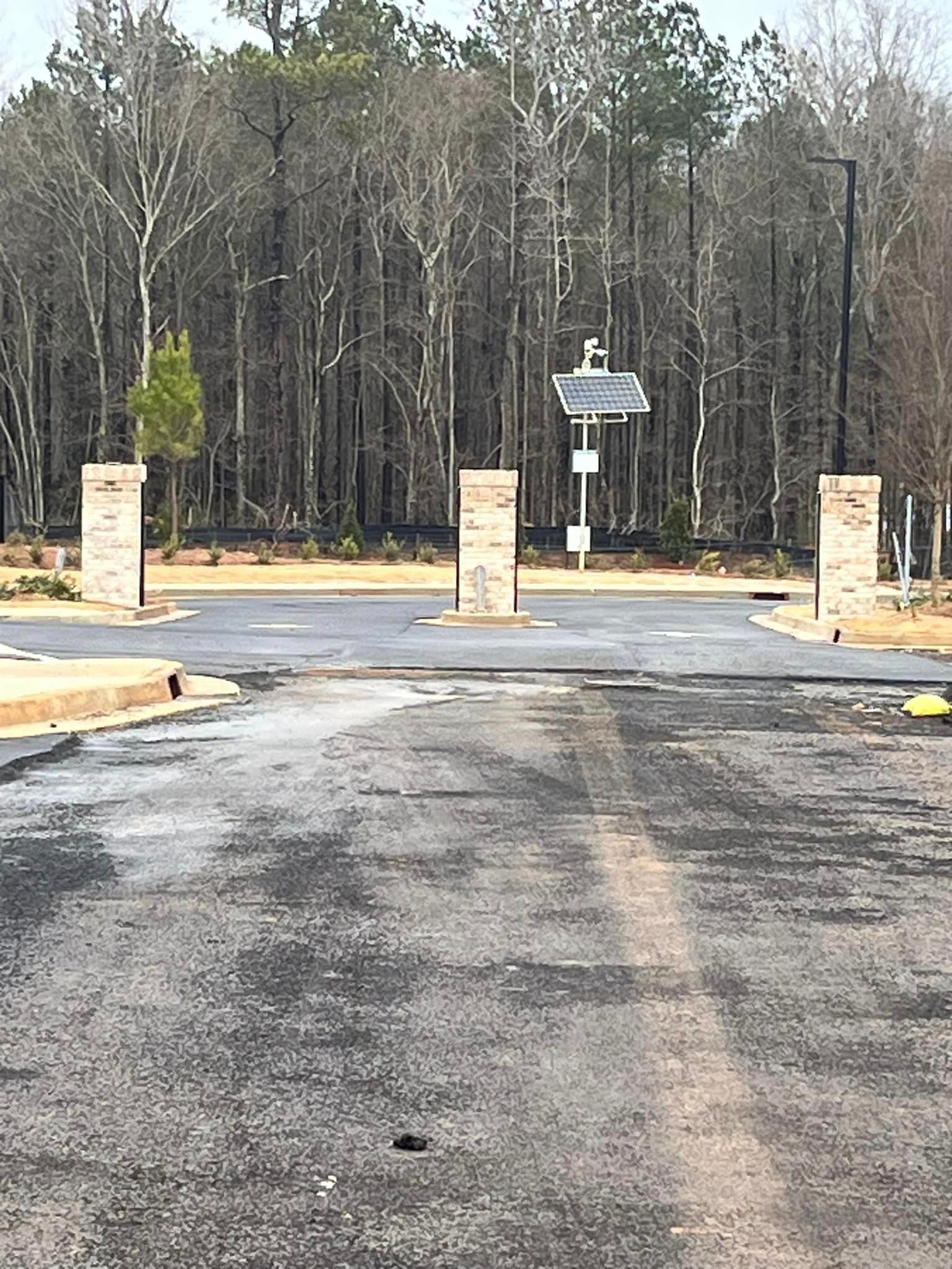 Entrance with brick columns and signage on a paved road, trees in the background.