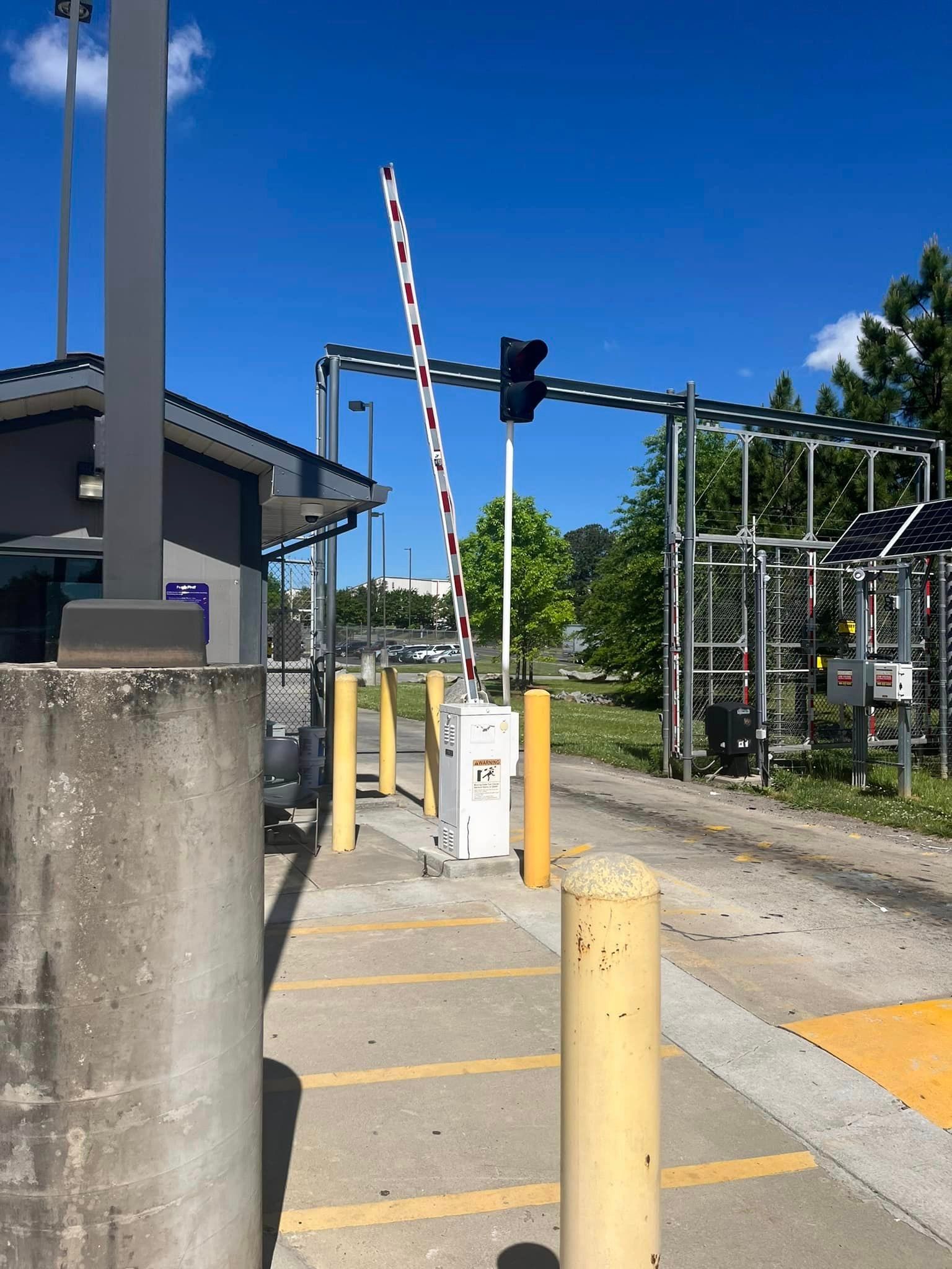 Entrance gate with a raised arm, a guard booth, and yellow bollards.