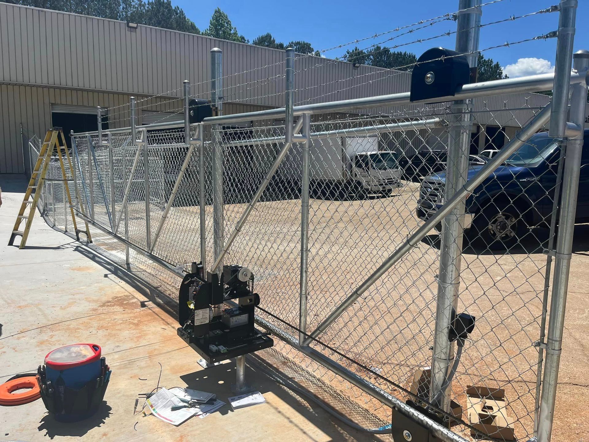 Chain link fence with barbed wire and automated gate in front of a building.