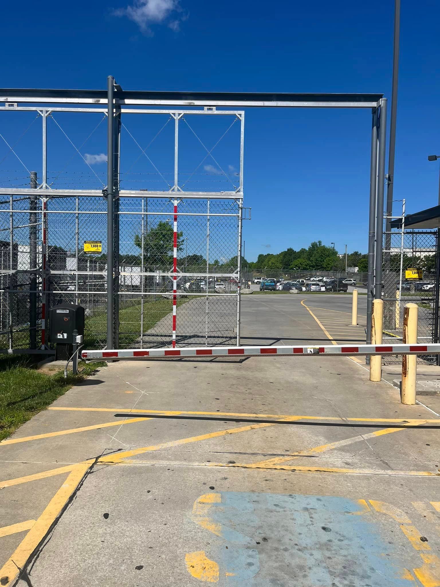 Chain link fence gate with raised white and red striped barrier; blue sky.