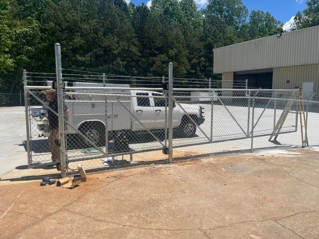A person installing a chain-link fence around a white truck parked in a lot. Building in the background.
