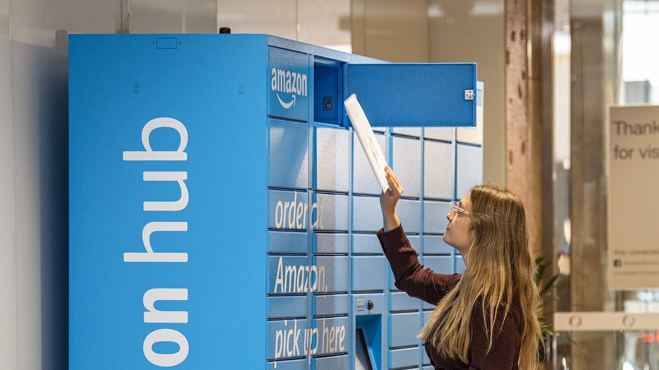 Woman retrieving a package from an Amazon Hub locker; blue lockers, modern setting.