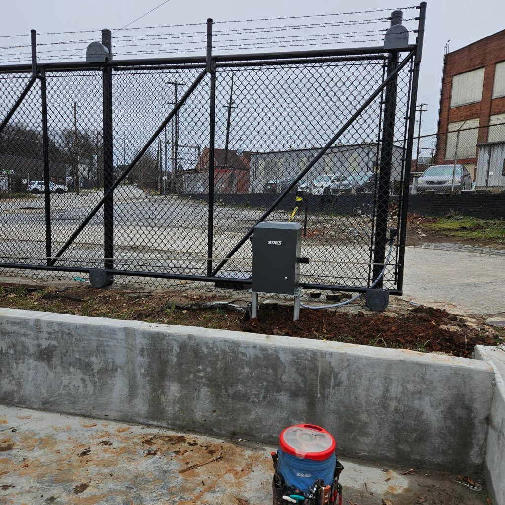 Black chain-link fence, concrete base, electrical box, red-blue bucket, and industrial setting.