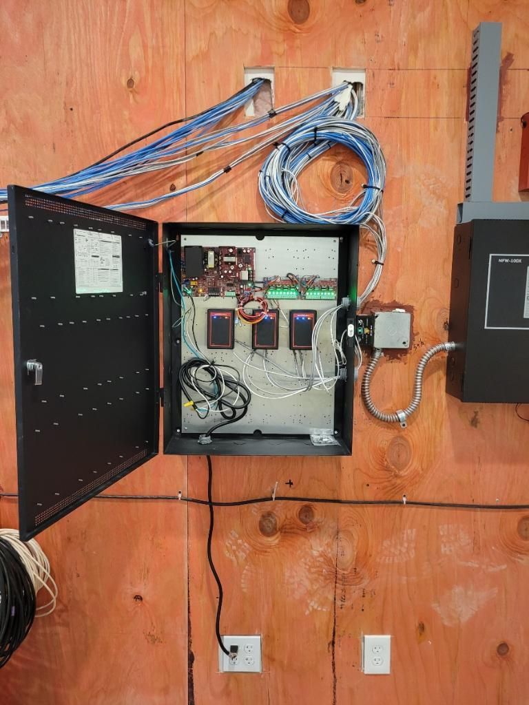 Open electrical cabinet on a wooden wall, containing wires, components, and a power outlet below.