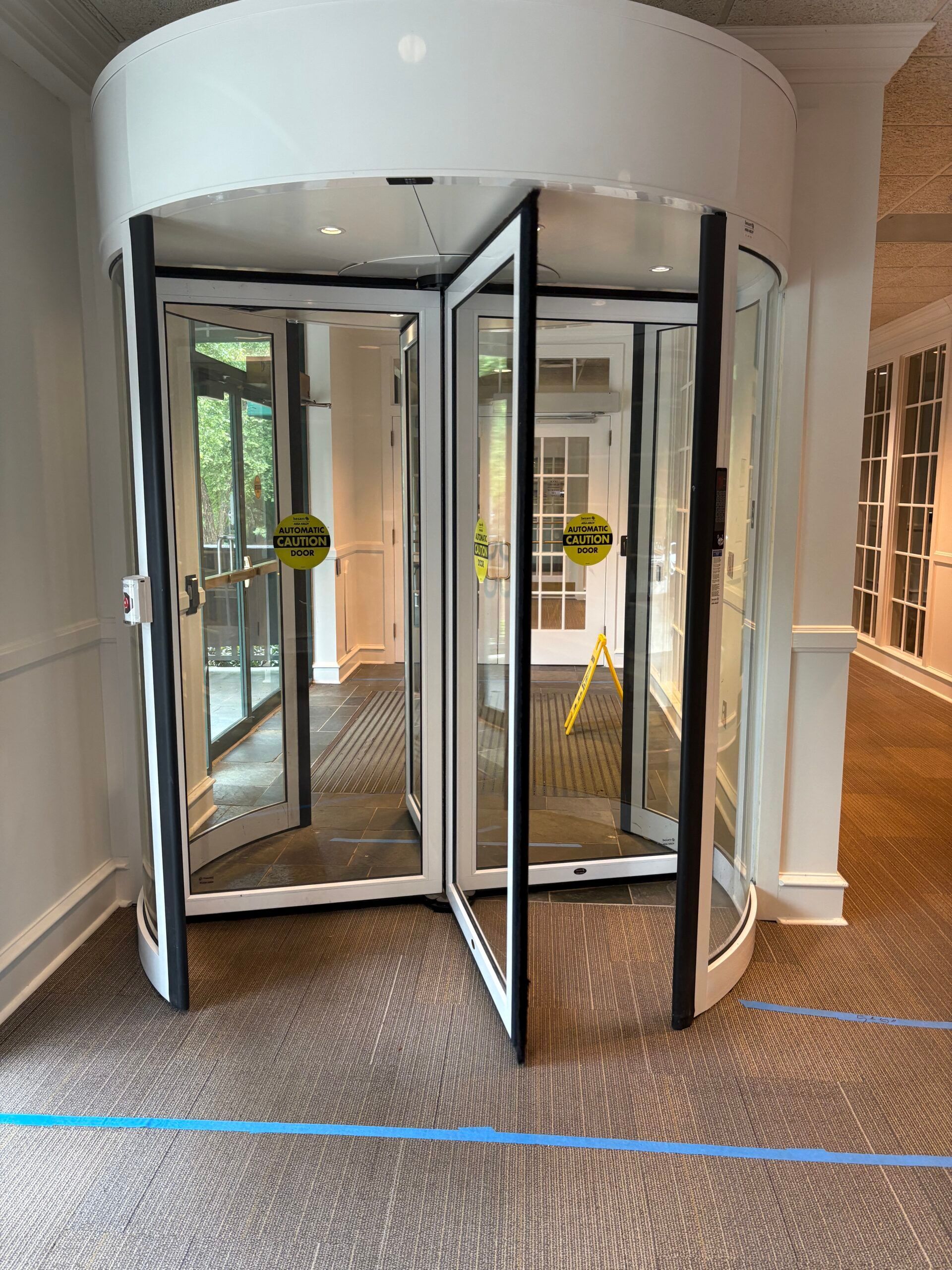 Revolving glass door in a building's entrance. Black frames, white trim, and a patterned carpet.