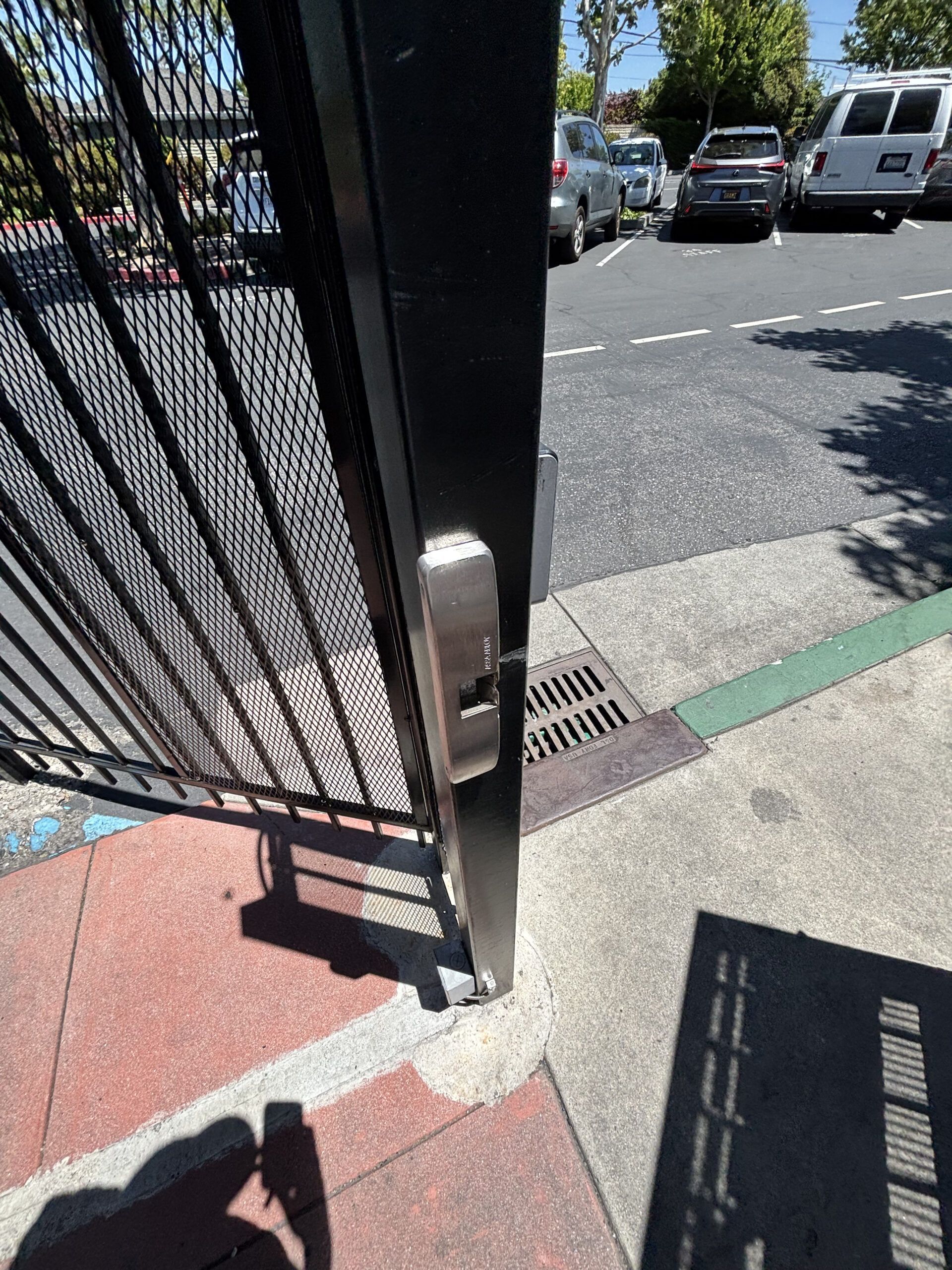 Black metal gate with a silver lock, located near a parking lot.