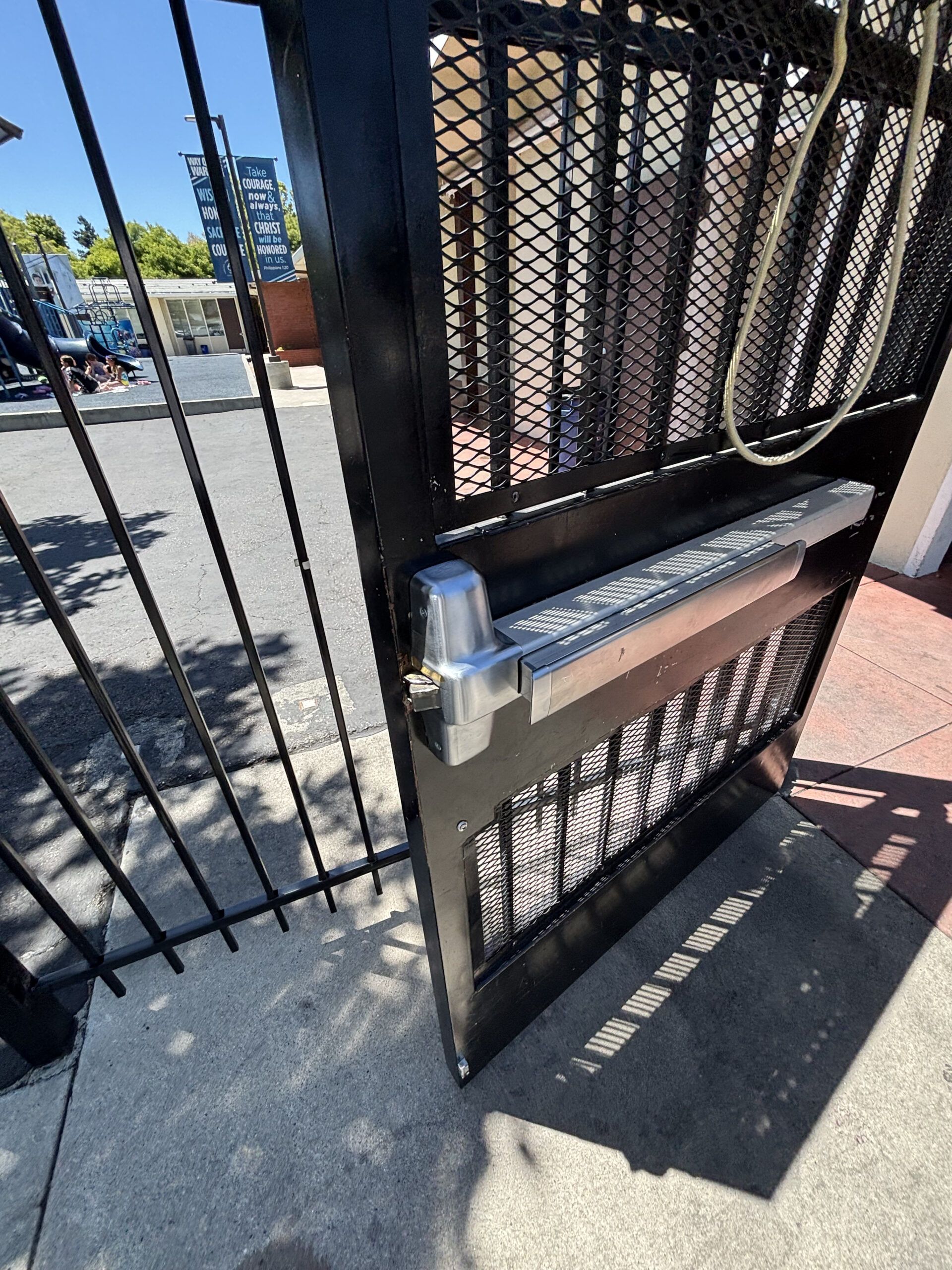 Black metal gate with an automatic opener, open on a sidewalk.