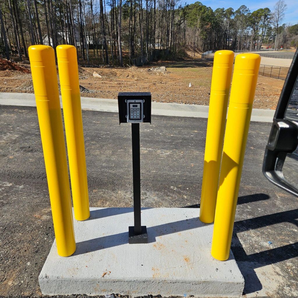 Yellow bollards surround an access keypad on a concrete base.