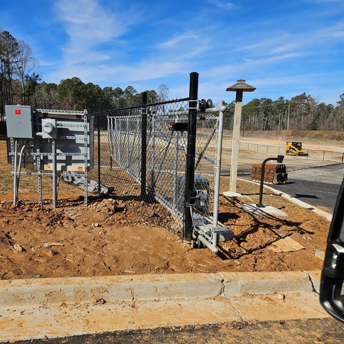 Outdoor electrical equipment with a fenced enclosure on a construction site. Blue sky overhead.