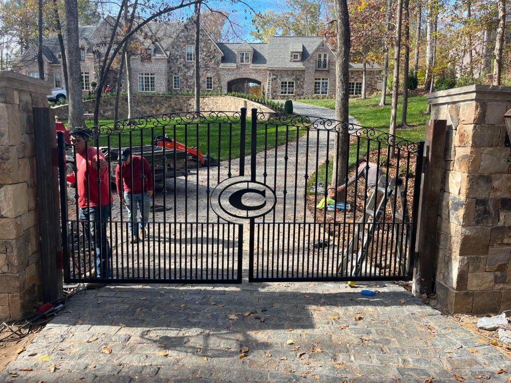 Private Residence - Marietta, Ga. Black wrought-iron gate with a logo, leading to a large house. Two people near gate.