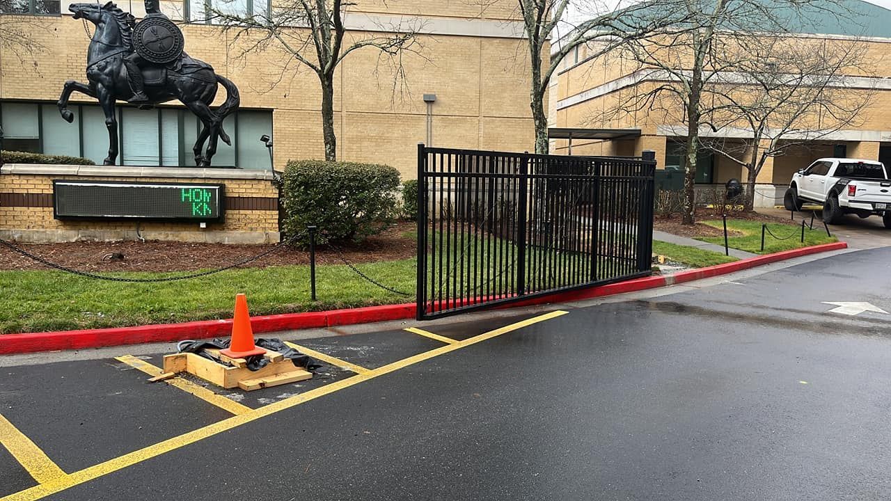 St Francis High School - Alpharetta, Ga Black metal gate with a partly visible building and bronze horse statue; parking lot with orange cone.