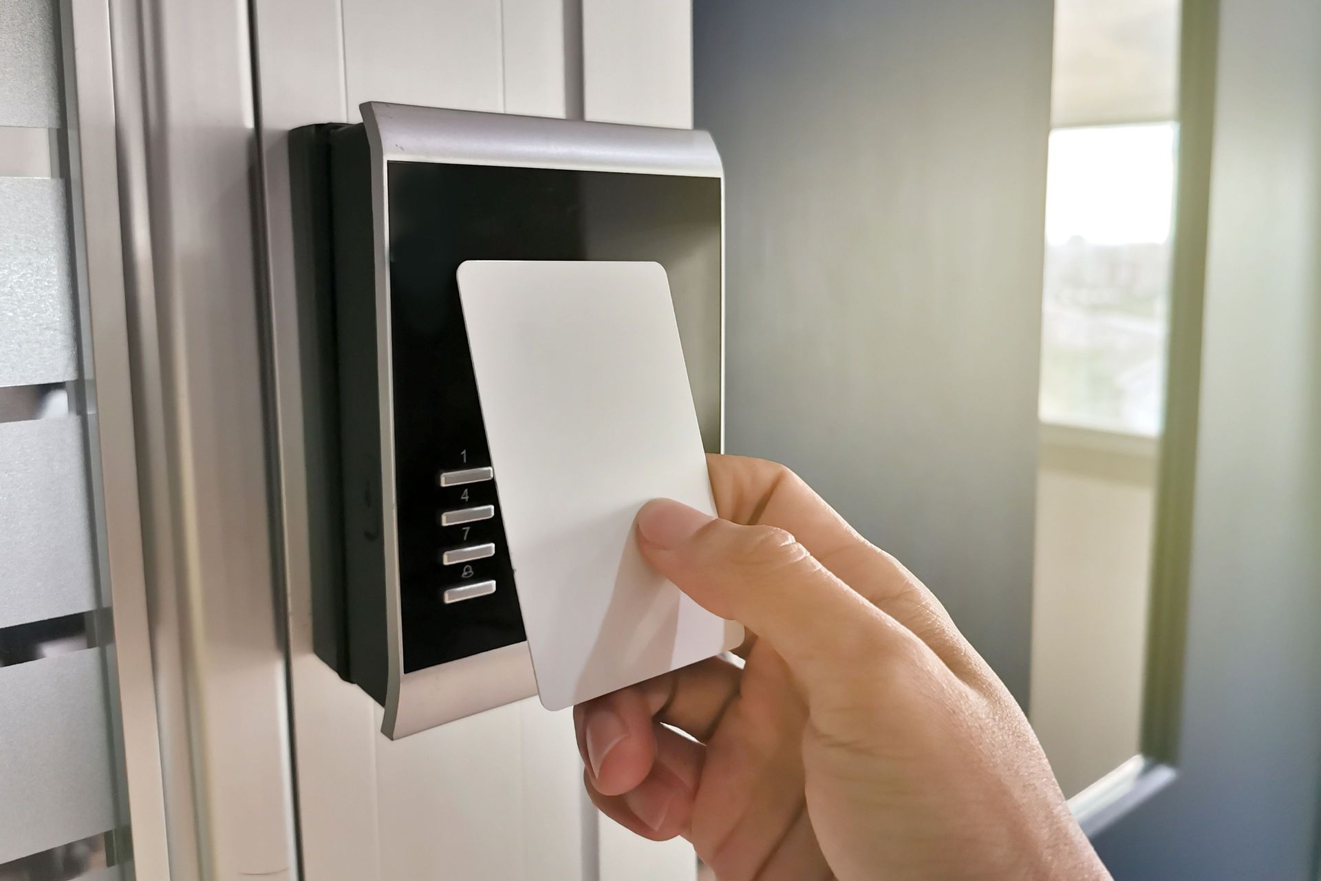 Hand holding a white access card near a door card reader.