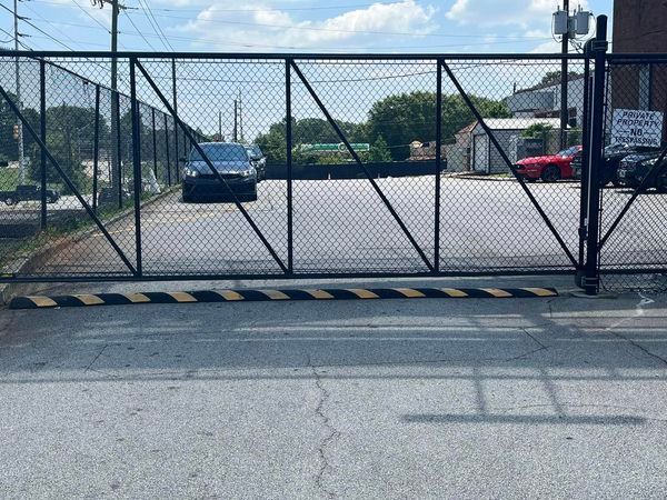 Tyler Perry Studios Black security gate with a car inside a fenced area; speed bump in front.