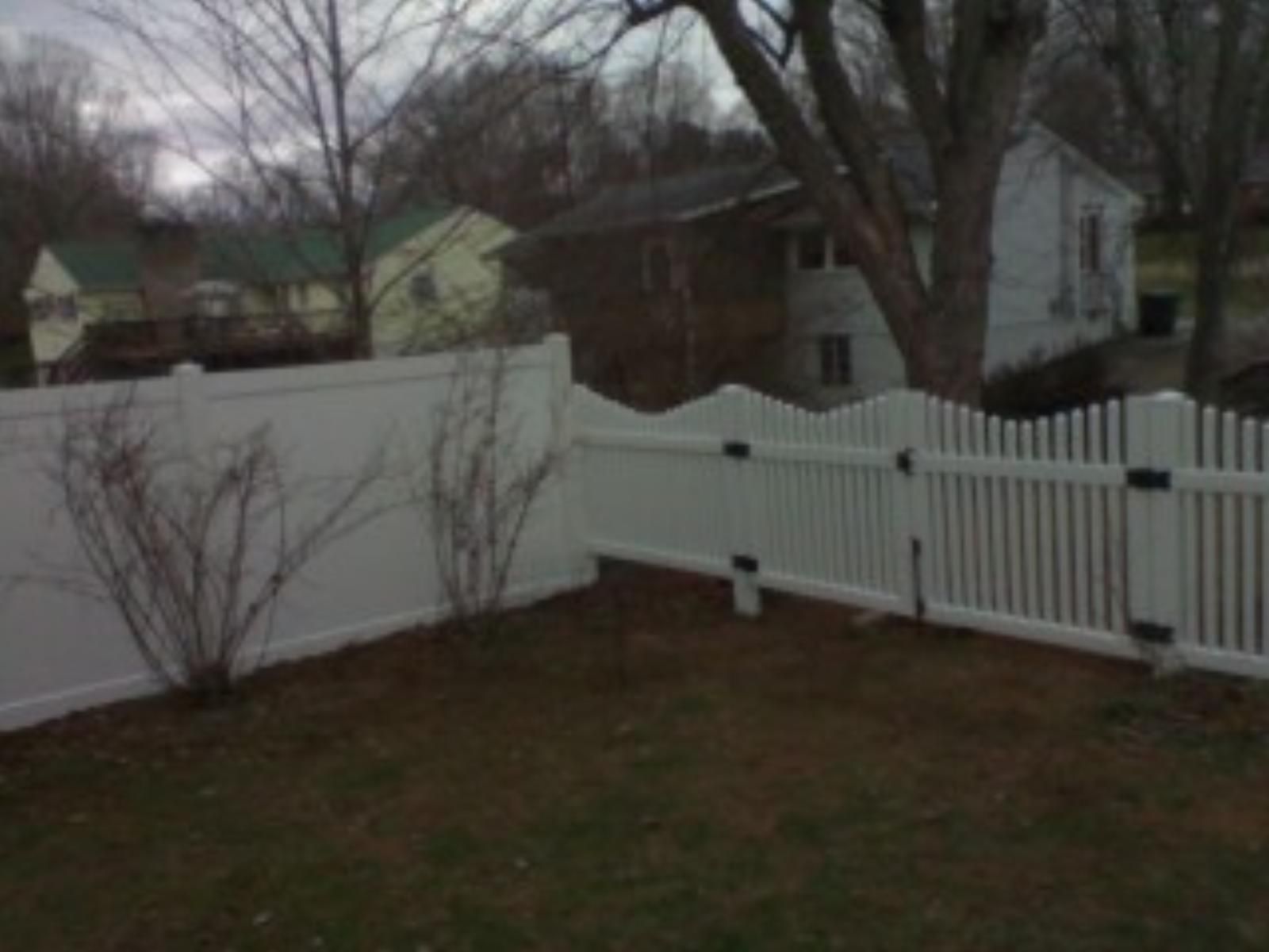 A white vinyl picket fence is in the backyard of a house