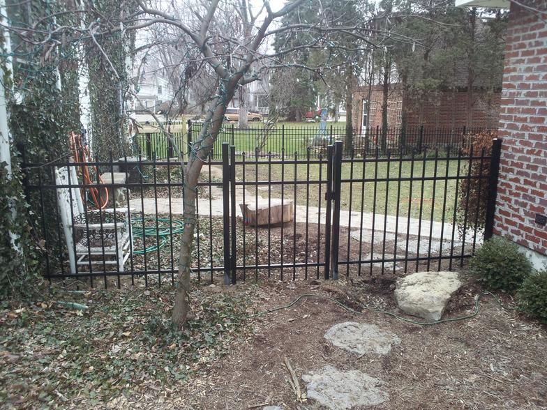 A black steel fence surrounds a backyard with a brick building in the background.