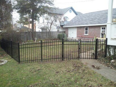 A black ornamental steel fence surrounds a lush green yard in front of a brick house.