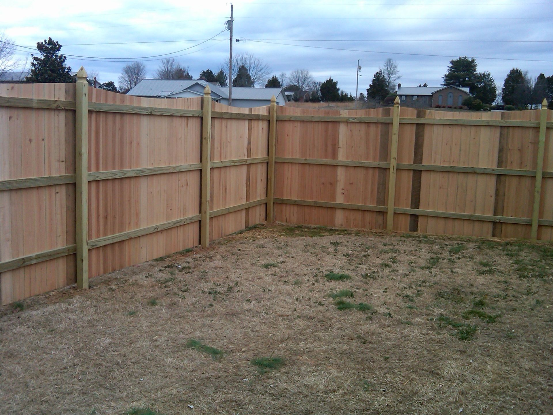 A wood privacy fence surrounds a grassy area in a backyard