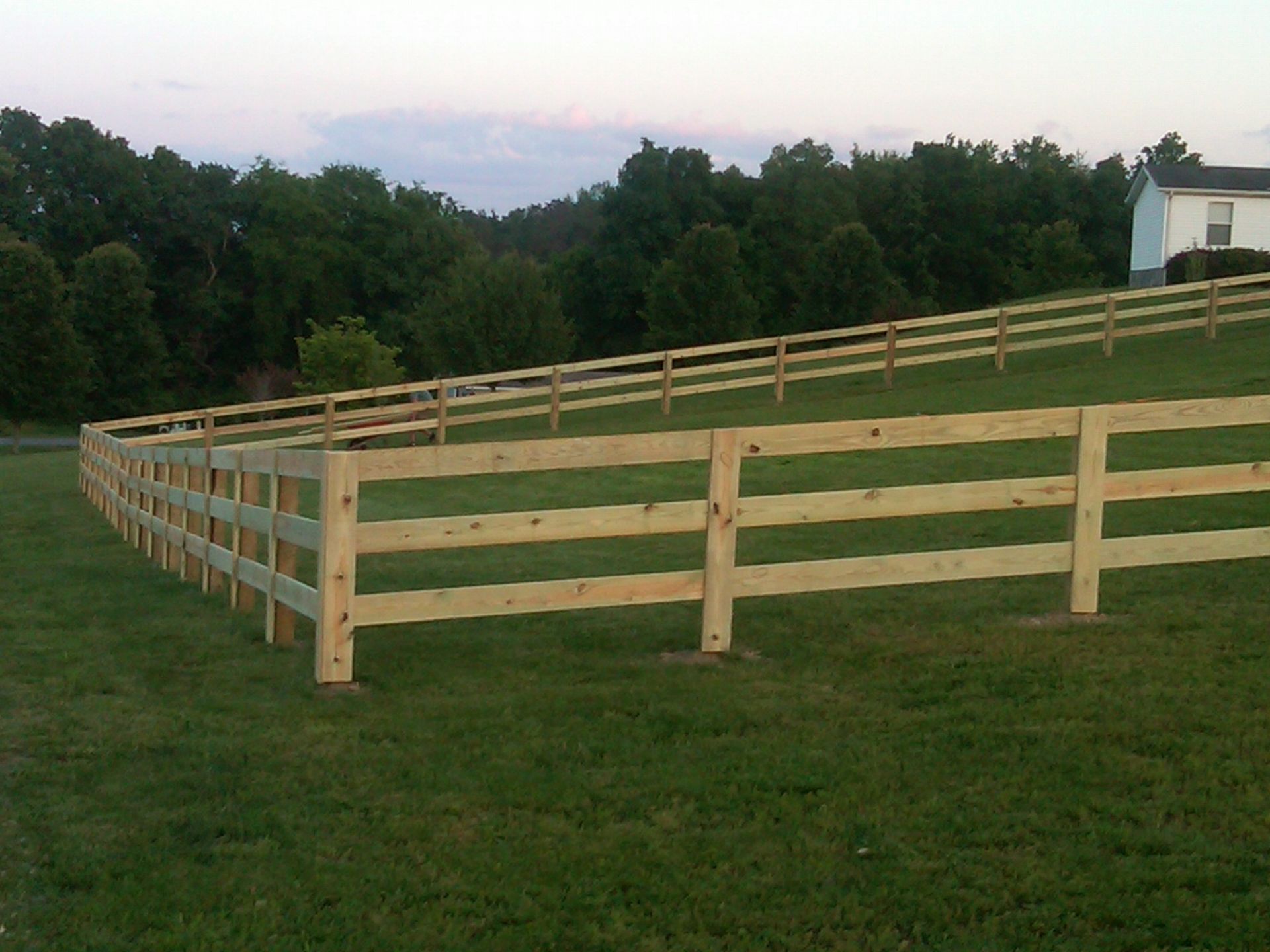 A split rail fence surrounds a grassy field with trees in the background
