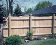 A man is installing a wood privacy fence in a backyard.