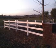 A split rail fence is sitting next to a brick wall.