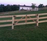 A split rail fence with a gate in a grassy field.