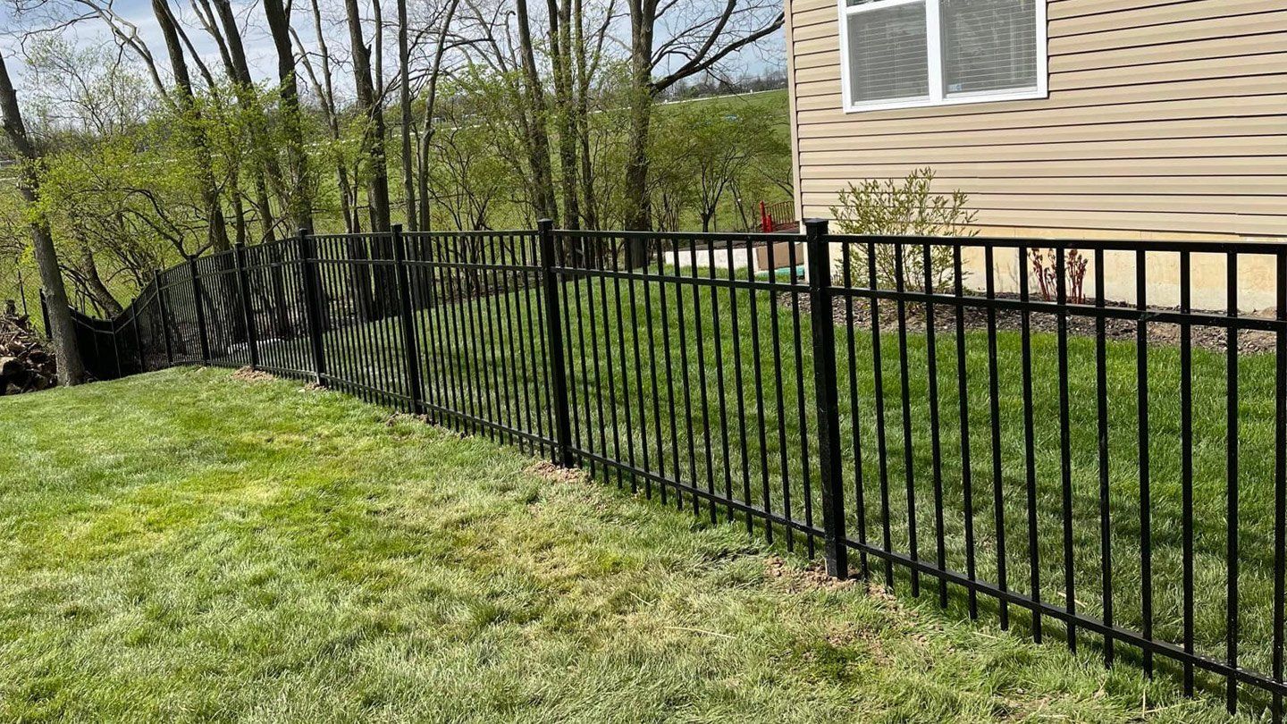 A black steel fence surrounds a lush green lawn in front of a house.