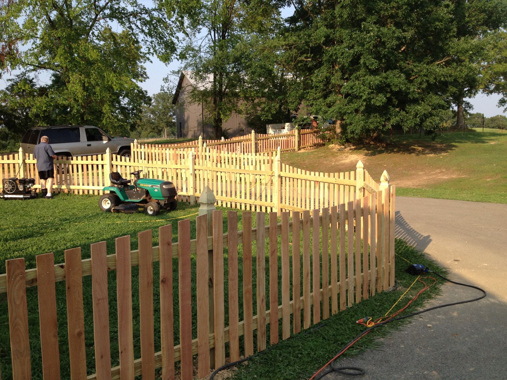 A green lawn mower is parked behind a wooden picket fence