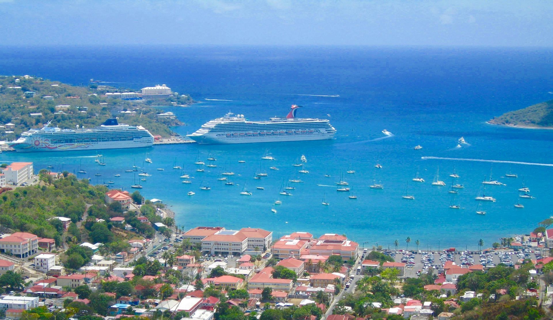 Two cruise ships are docked in a harbor surrounded by boats