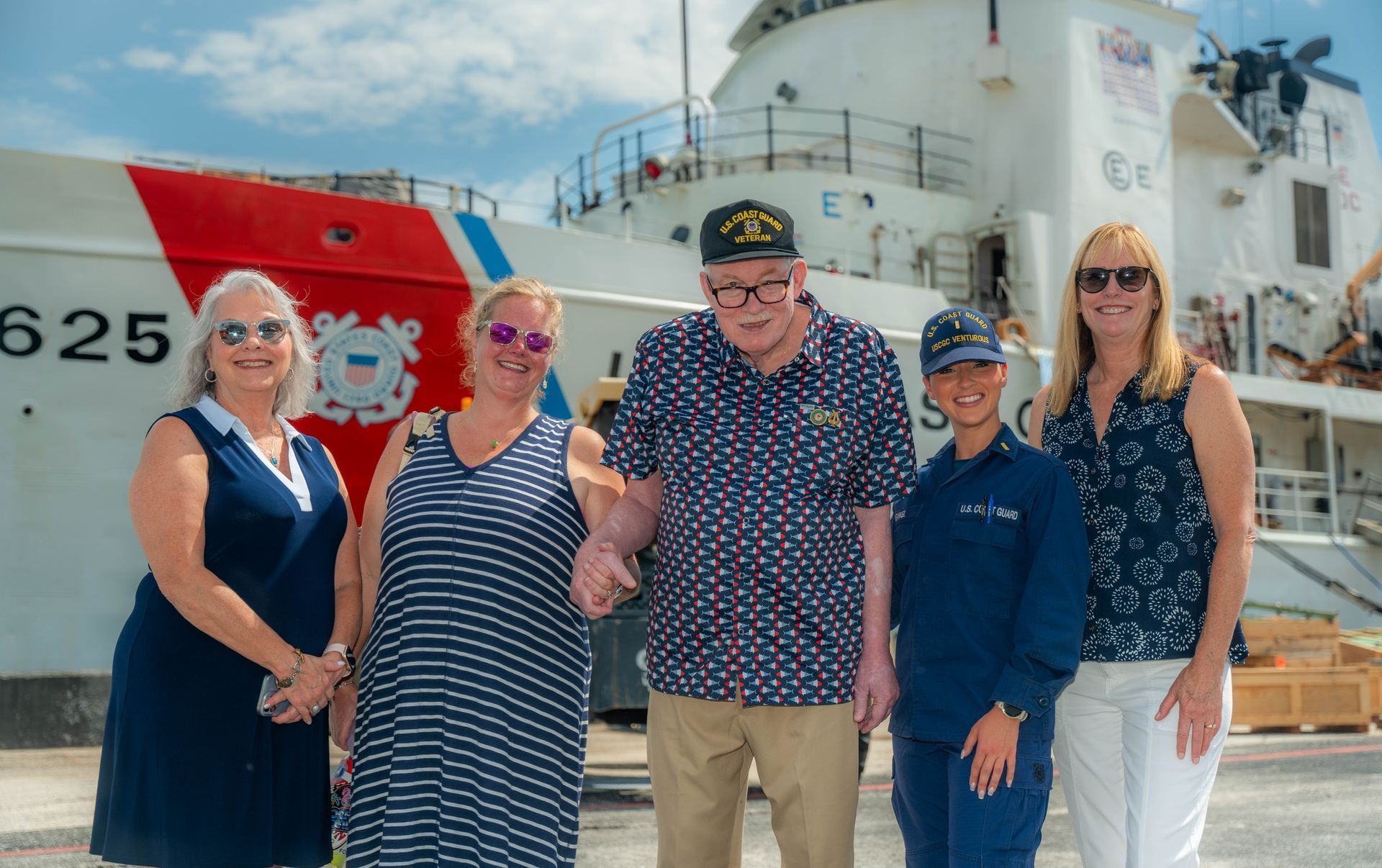 Five people, including a veteran, pose in front of a Coast Guard ship.