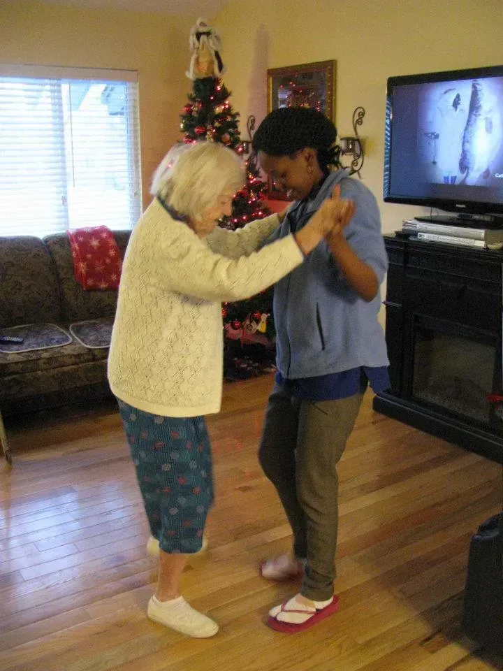 An older woman dances with a younger woman in a living room with a Christmas tree.