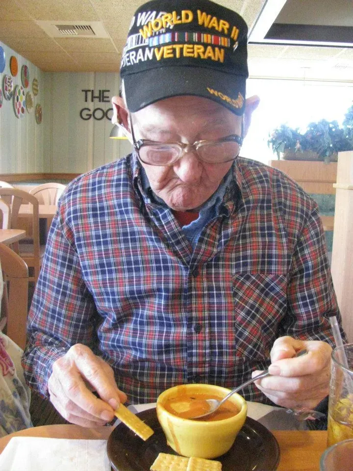 Elderly man in World War II veteran hat eating soup in a restaurant.
