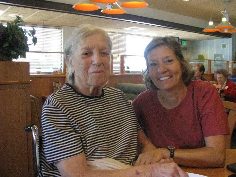 Two women smiling at a table in a restaurant, one older with striped shirt, the other younger with red shirt.