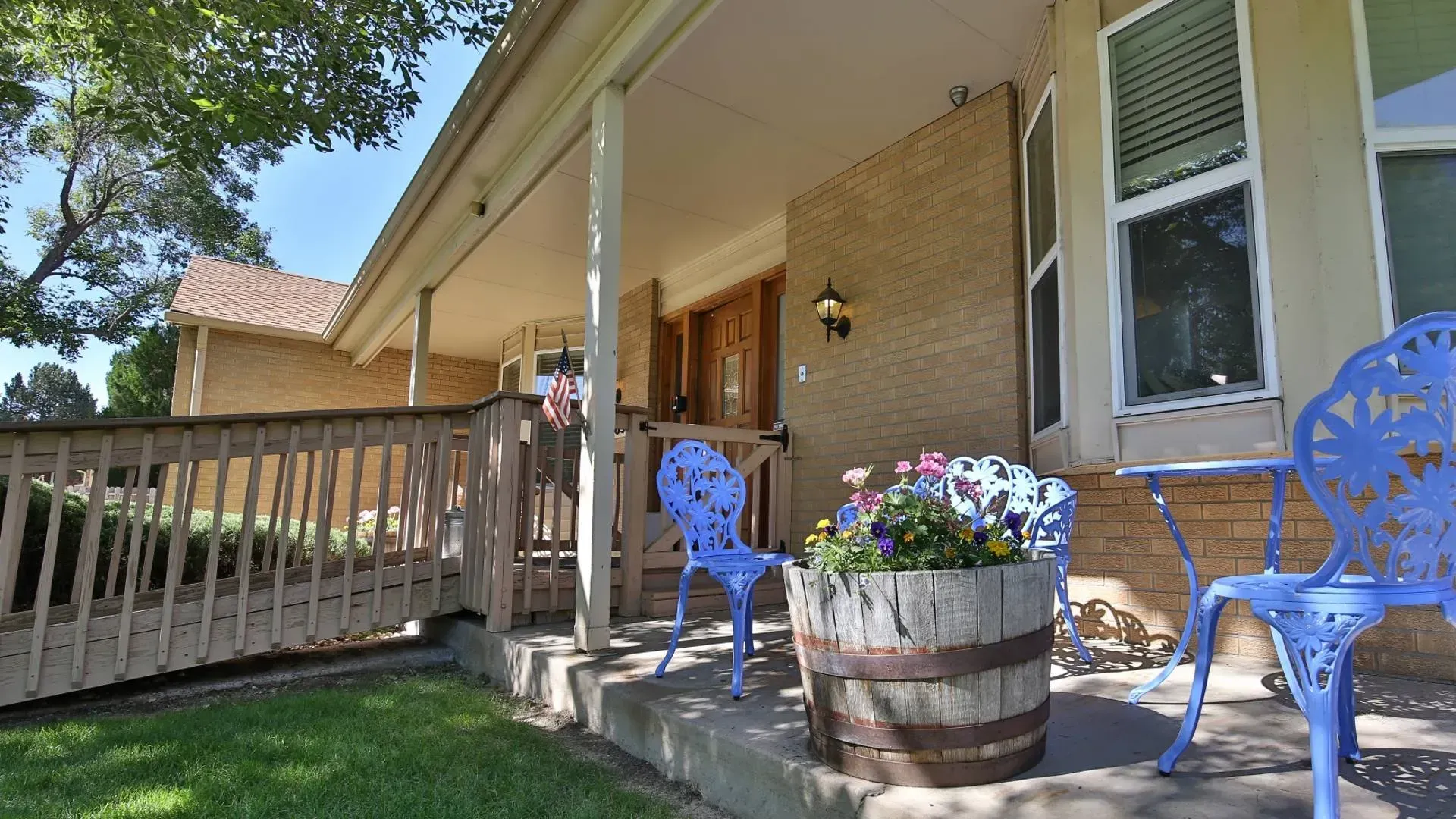 Blue chairs and a barrel planter on a porch of a brick house.