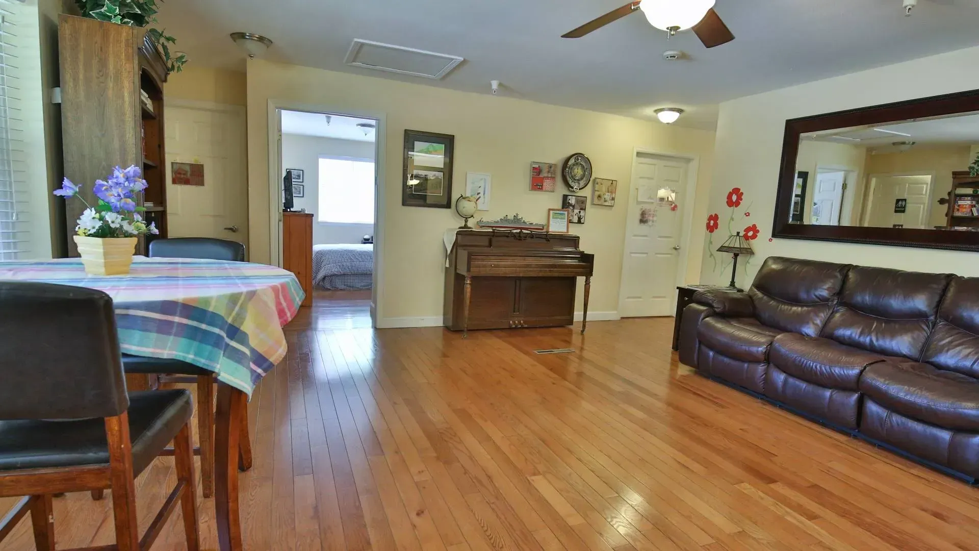 Living room with hardwood floors, dining table, leather couch, and a piano.