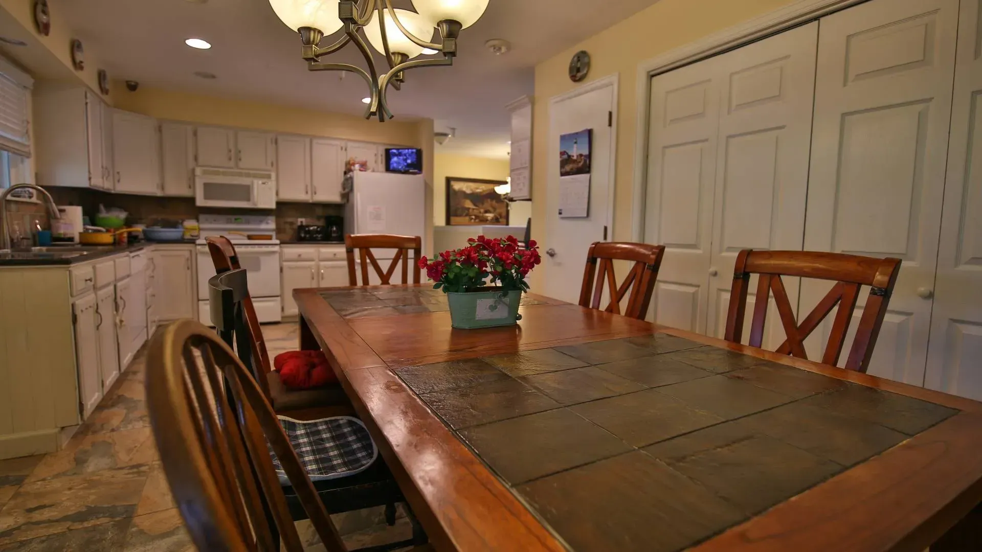 Dining room with wooden table, chairs, kitchen in the background, and a chandelier.