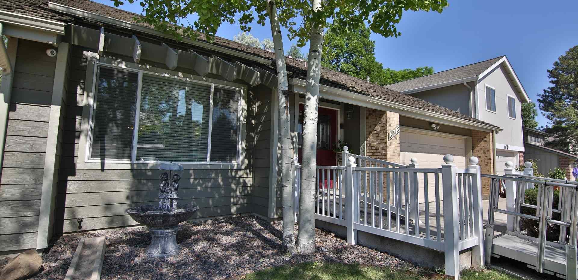 House exterior with stone and white siding, porch, fountain, and trees under a blue sky.