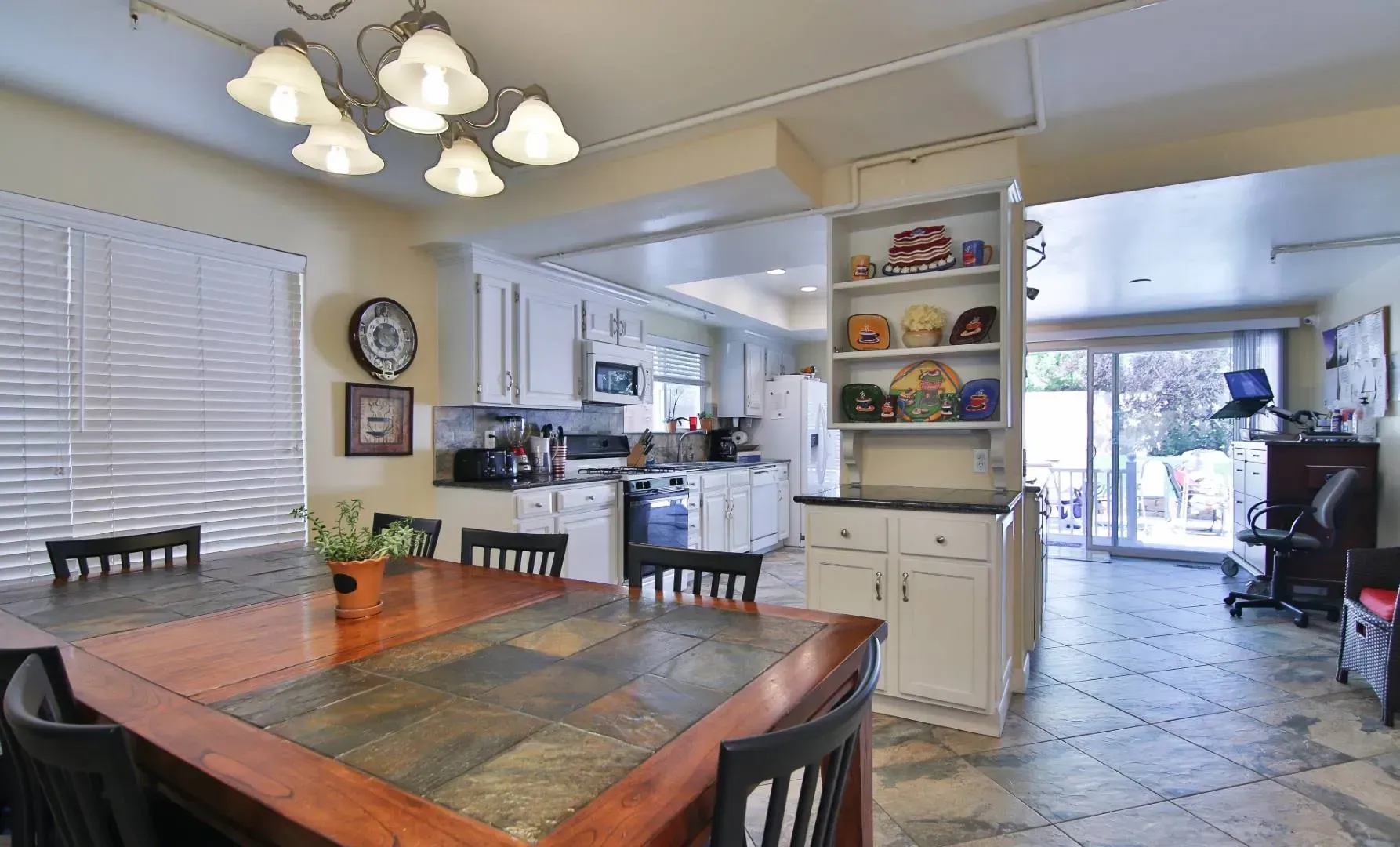 Dining room with a wooden table, open kitchen, and a view of the patio.