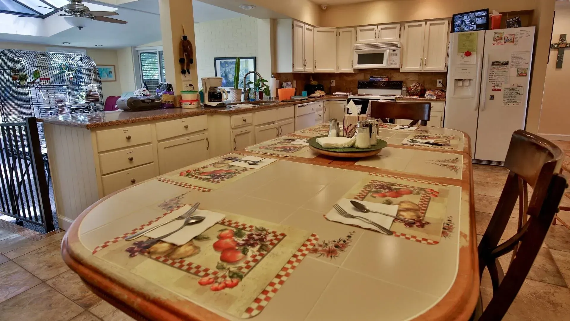 Kitchen with large table set for a meal; cream-colored cabinets and appliances; bright lighting.