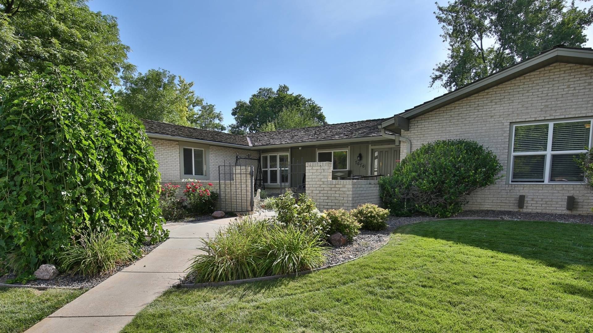 A house with a light-colored brick facade, green lawn, and walkway leading to the front door.