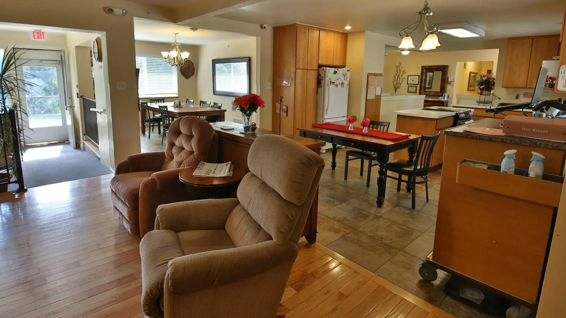 Cozy living room with recliner chairs, dining area, and kitchen; likely in a senior living facility.