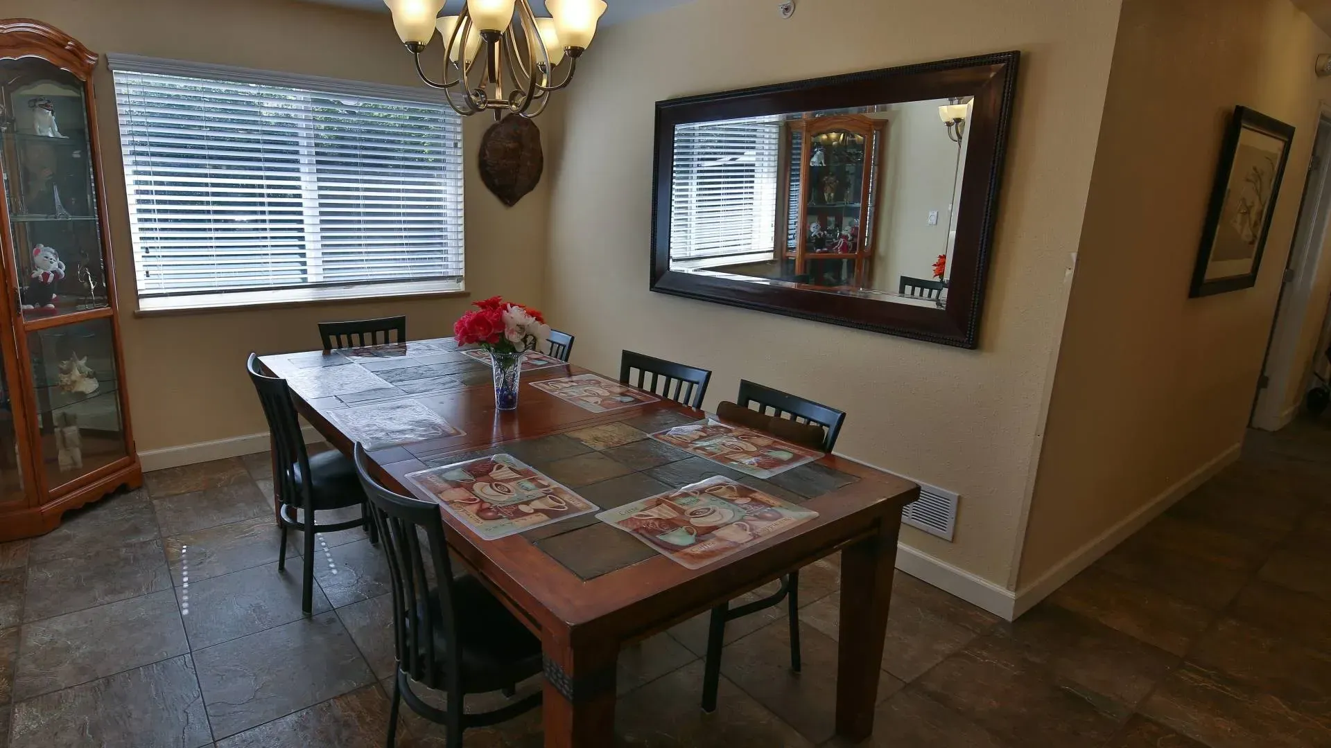 Dining room with table set for six, mirror, and decorative cabinet.