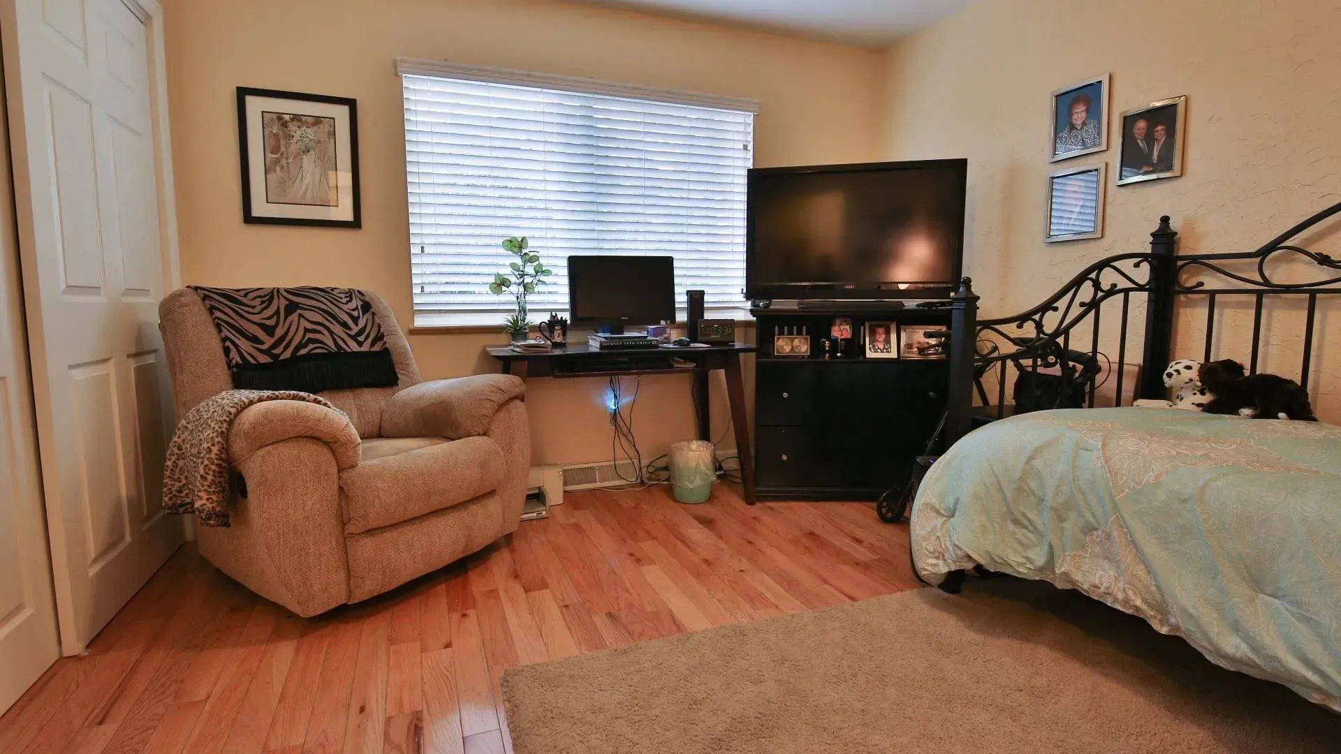 Bedroom with bed, recliner, desk, TV, and window with blinds.