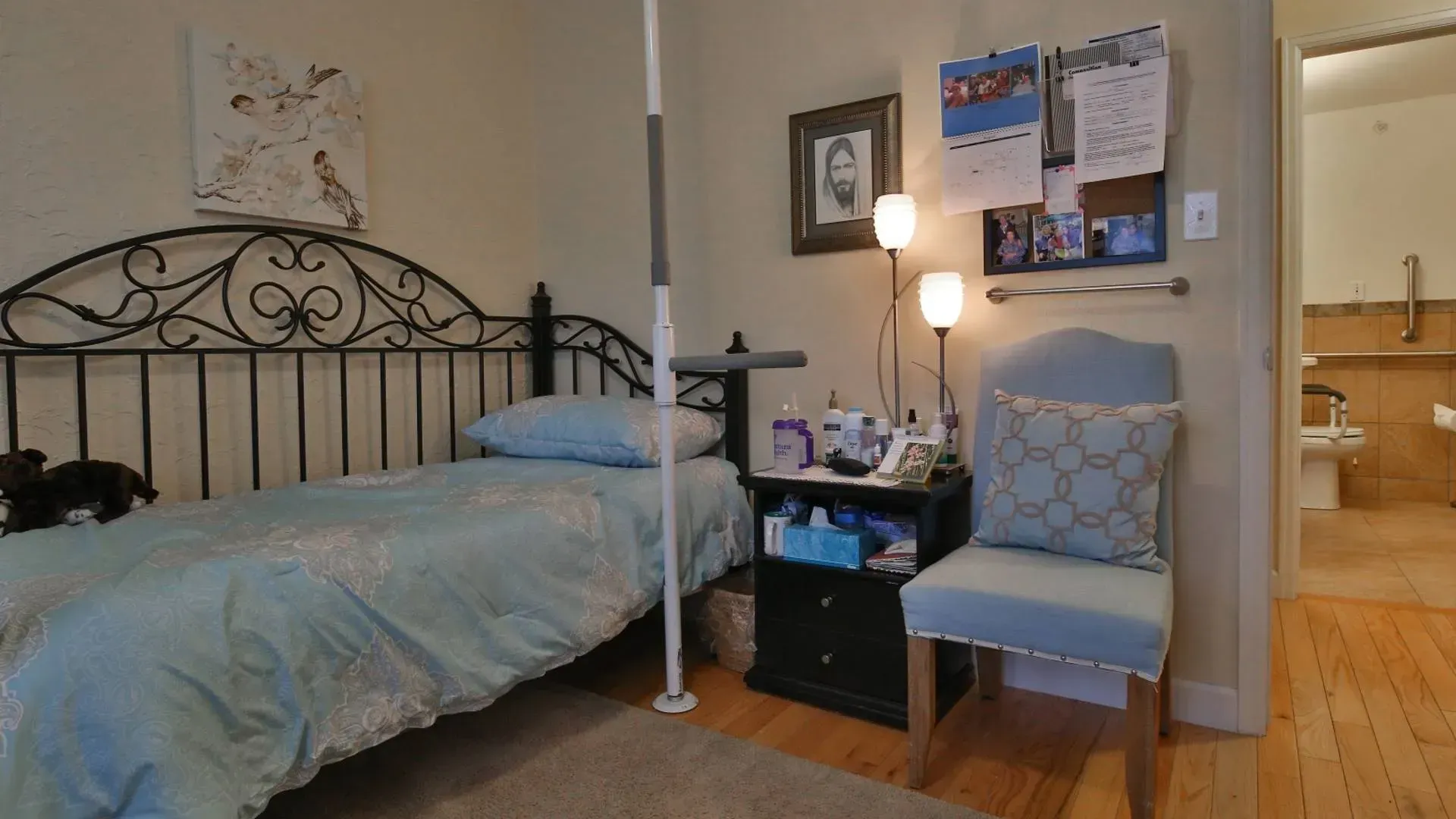 Bedroom with bed, nightstand, chair, pole, and open bathroom door.