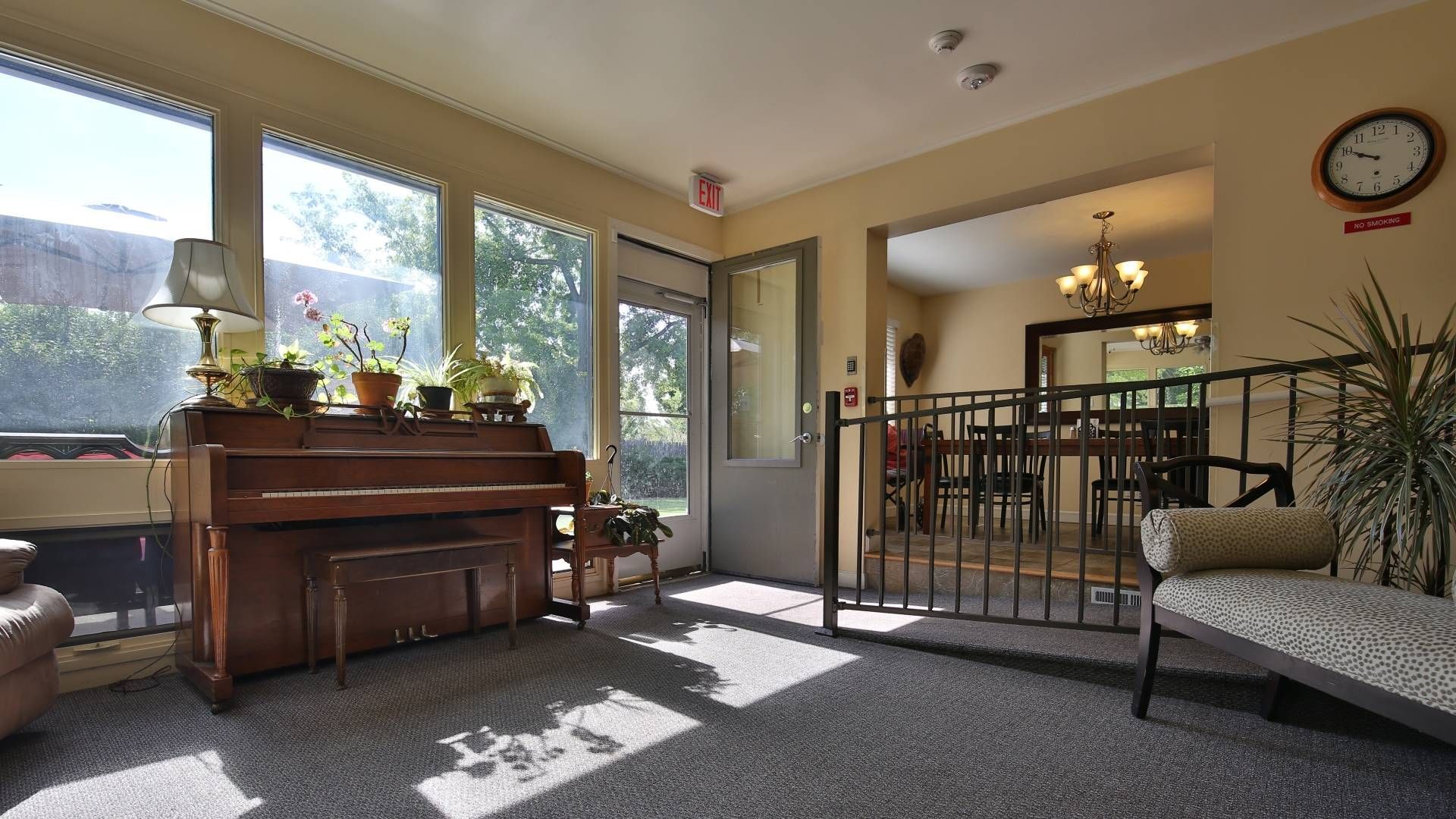 Sunroom with piano, plants, seating, and a view into a dining area.